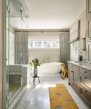 A large bathroom with marble floors, a glass shower, a yellow runner, and a gold animal sculpture