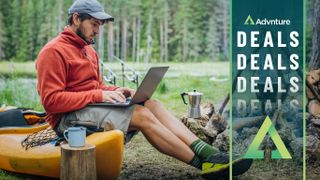 Man sitting on kayak at campsite working on laptop