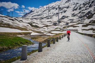 A male cyclist in a pink cycling jersey rides on the cobbles of the Gotthard Pass