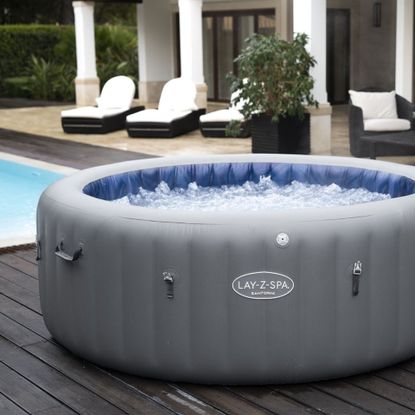 A grey inflatable Lay-Z-Spa hot tub on decking by a pool with sun loungers in the background