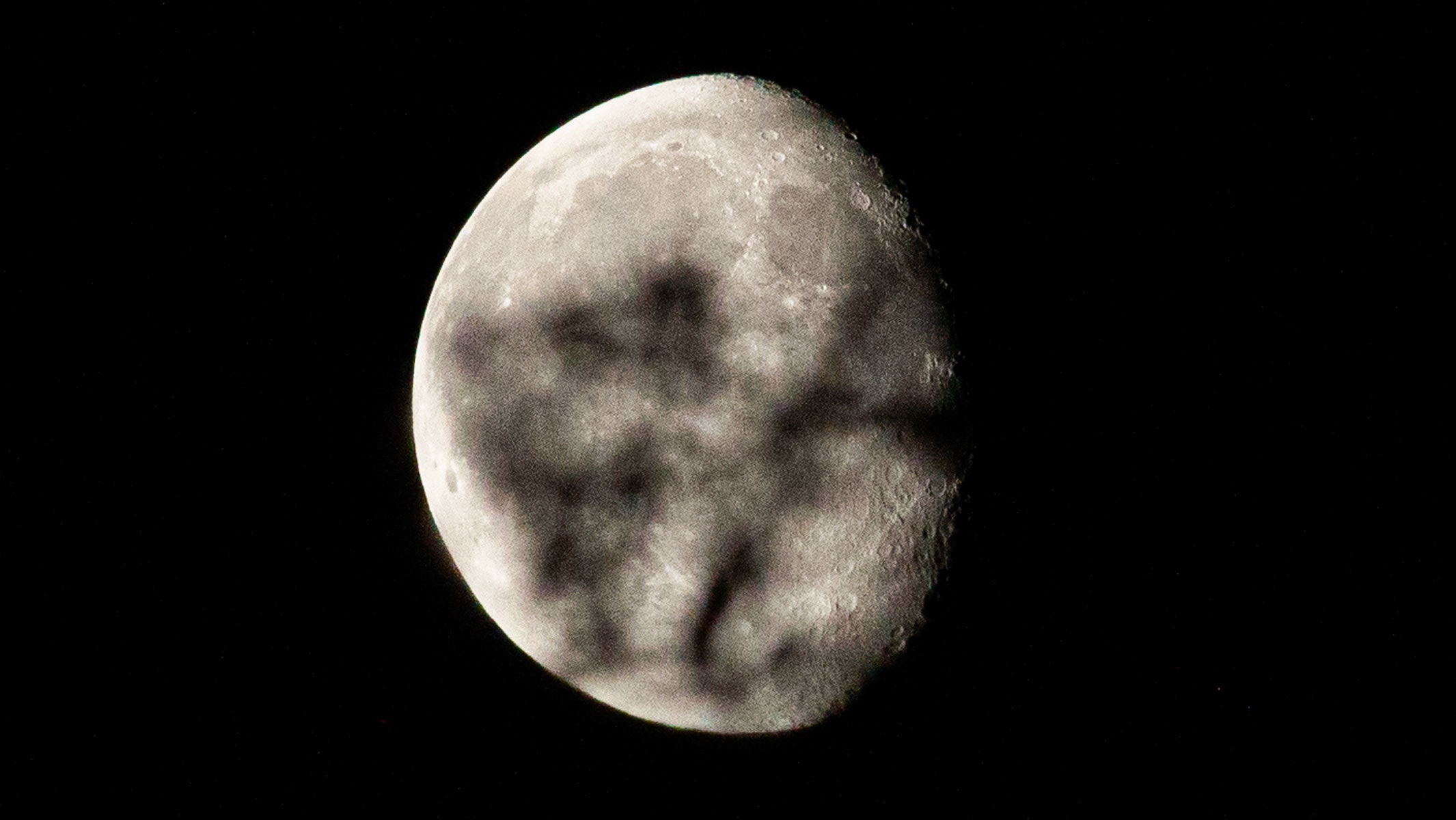 An in-focus waning gibbous moon with an out-of-focus branch in the way.
