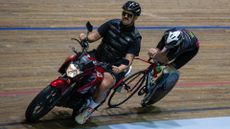 Kyleigh Manners riding a derny motorbike on a wooden velodrome track pacing a rider behind him 
