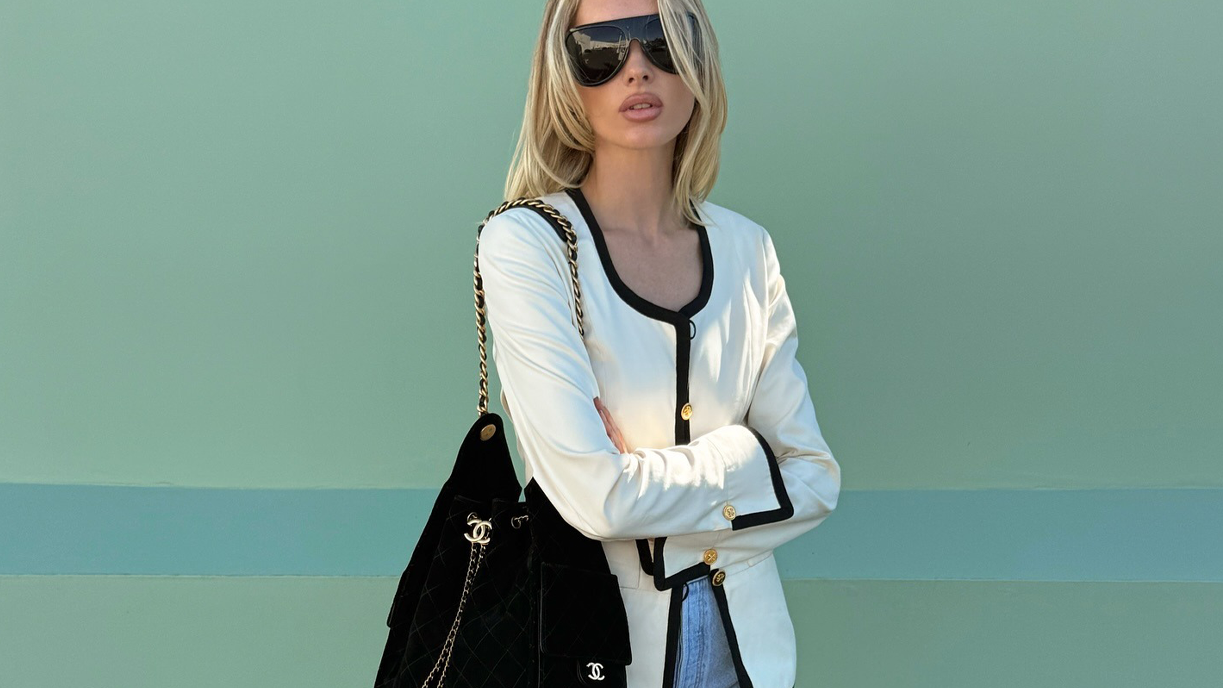Photo of Elsa Hosk wearing white jacket with black trim, black Chanel bag, and light wash jeans.