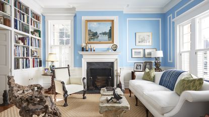 A library with light blue walls, marble fireplace and a bookcase wall