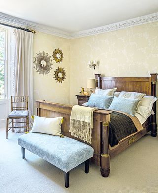 bedroom with tradiitional style wooden bed and pale wallpaper with sunburst mirrors