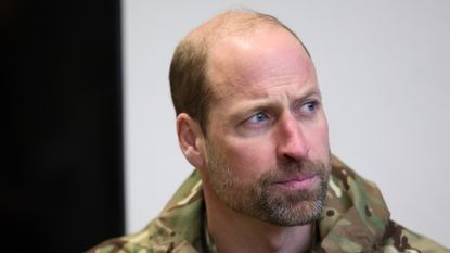 Prince William, looking serious and bearded, in army fatigues