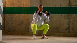 Woman performs squat holding dumbbells by her shoulders