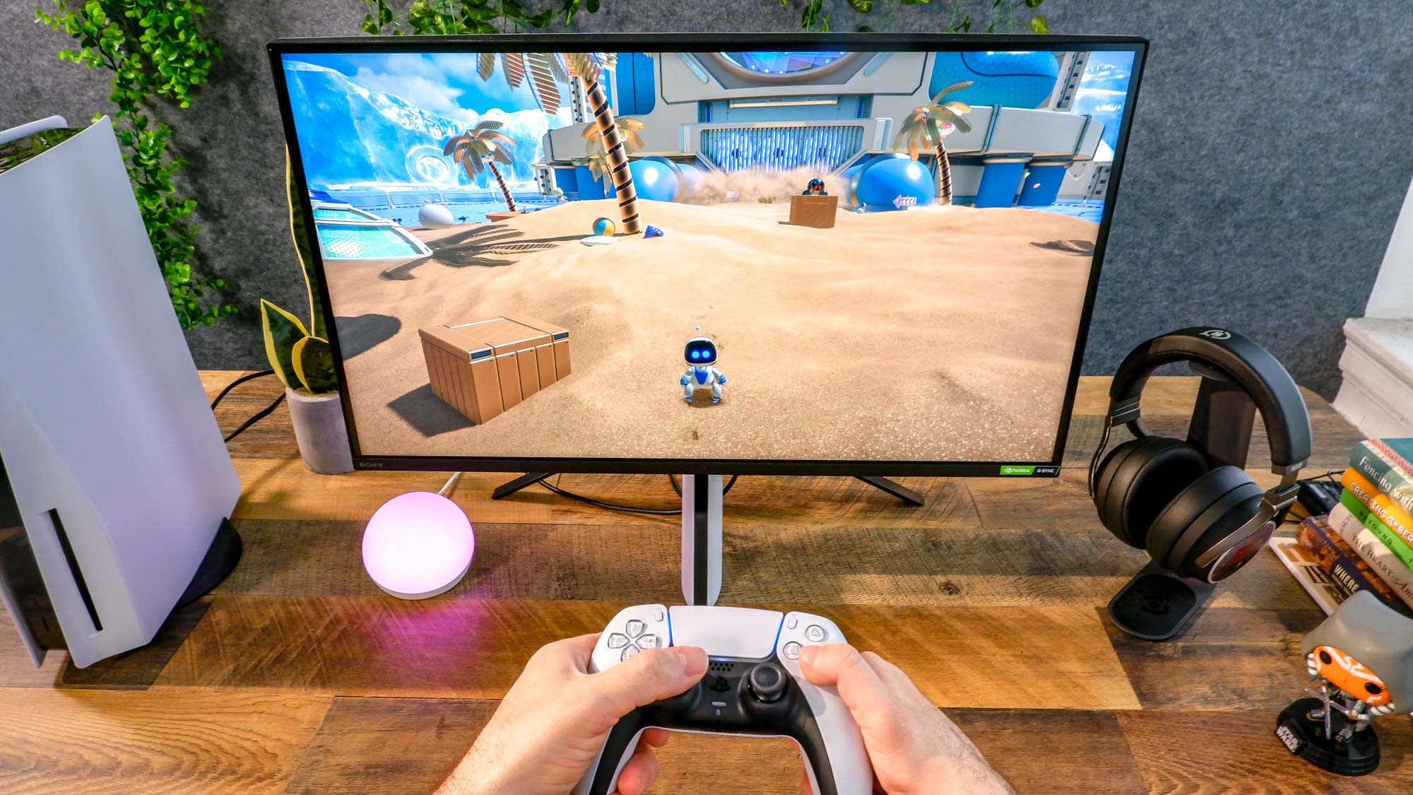 Sony Inzone M9 on a desk with hands in frame holding controller, a PS5 game onscreen