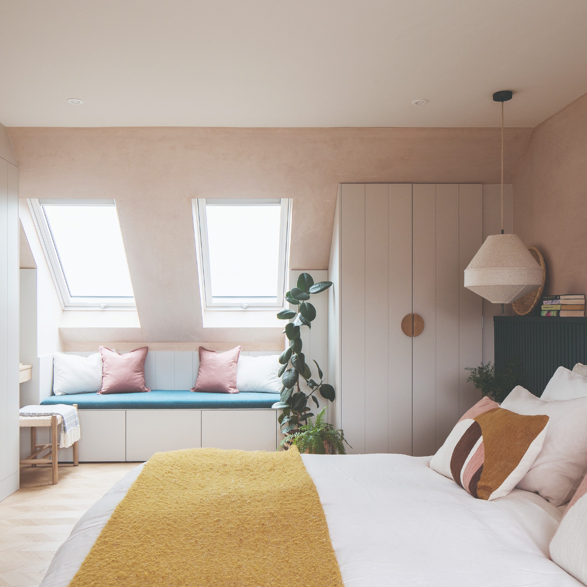 A bedroom painted in plaster pink with a limewash finish on the walls and a white ceiling with built-in wardrobes in off-white