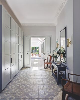 Hall with cabinetry, side table and mirror above and patterned floor tile