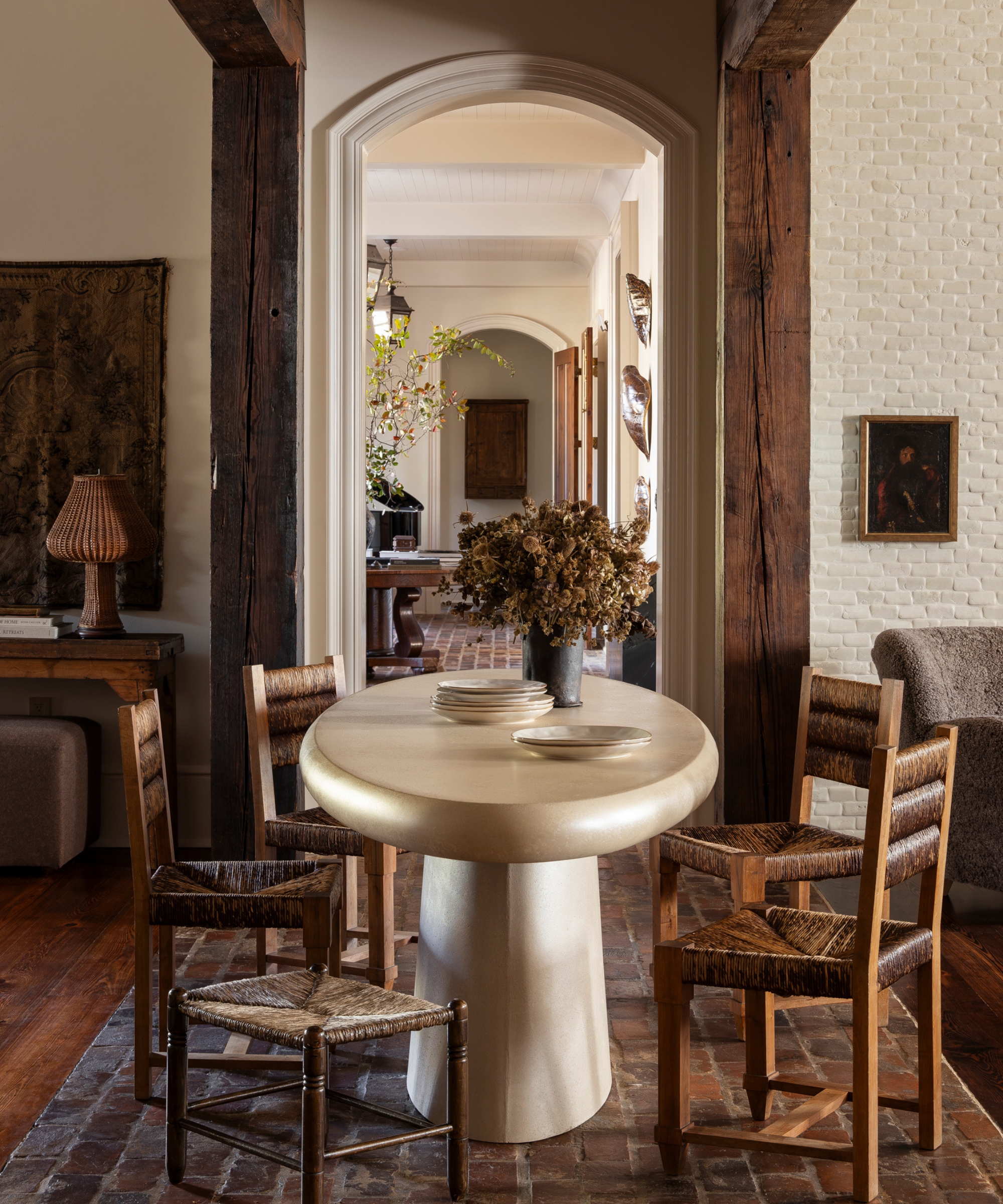 A small, four-seater table set up in a moody kitchen, featuring a white table and wooden chairs with woven seats and backrests