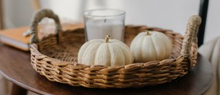 A wicker tray with white pumpkin decorations and a candle.