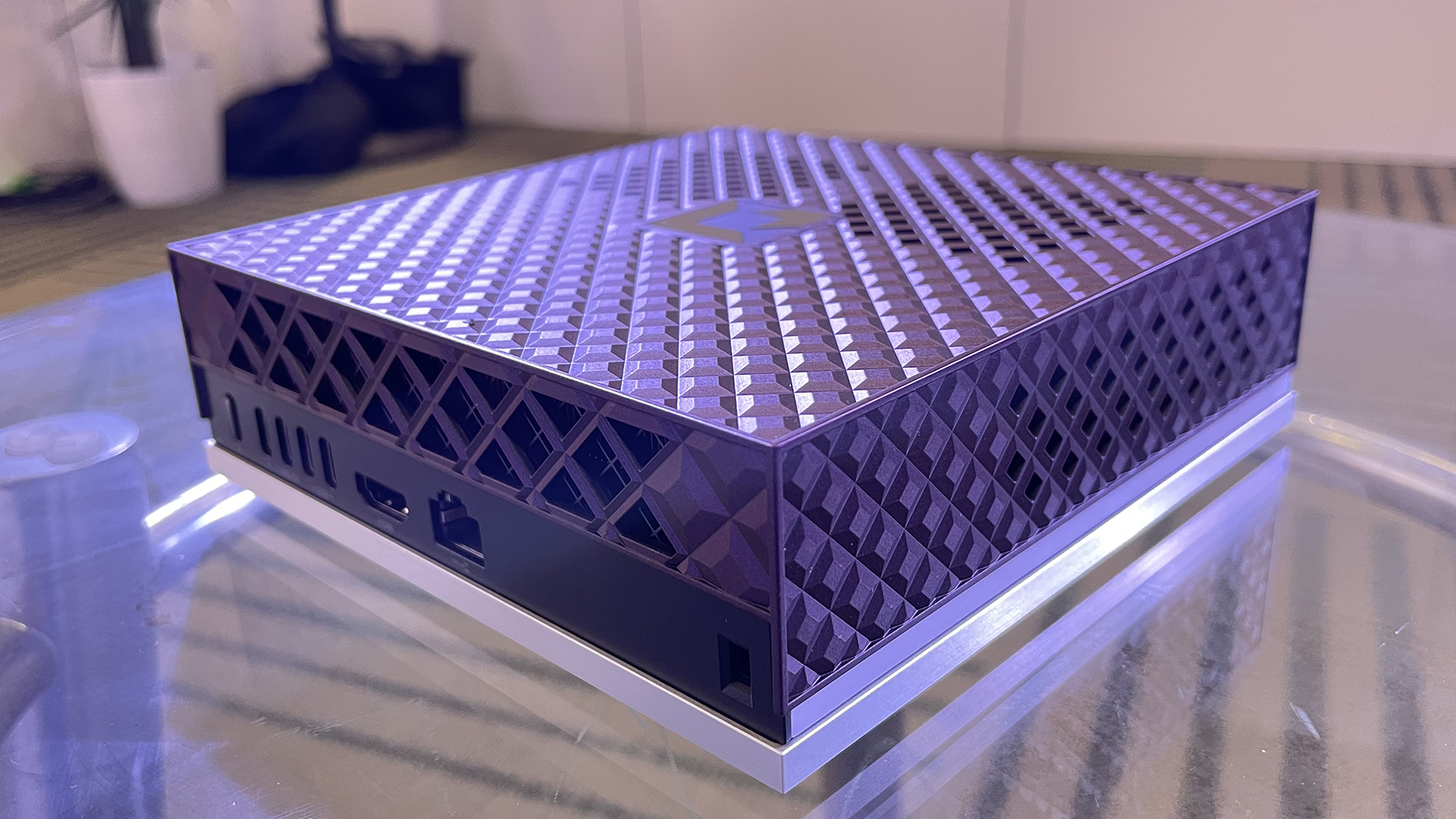 A close up, angular view of AMD Ryzen AI Halo. It has a purplish tint on a latticework exterior. There are several ports along the lefthand side, including Ethernet, HDMI, and USB