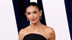 Image of Demi Moore with her black straight hair tied into a sleek ponytail and wearing a black strapless top, crystal drop earrings and red lipstick