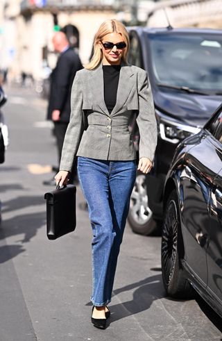 Kendall Jenner wears a gray jacket, black top, blue jeans, black flats, and a black top-handle bag.