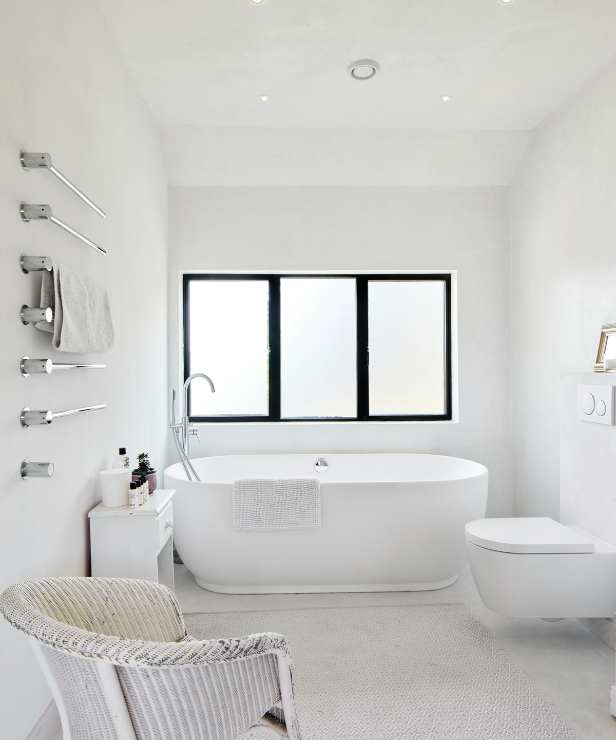 White bathroom with freestanding bath and three windows with a black trim in the background