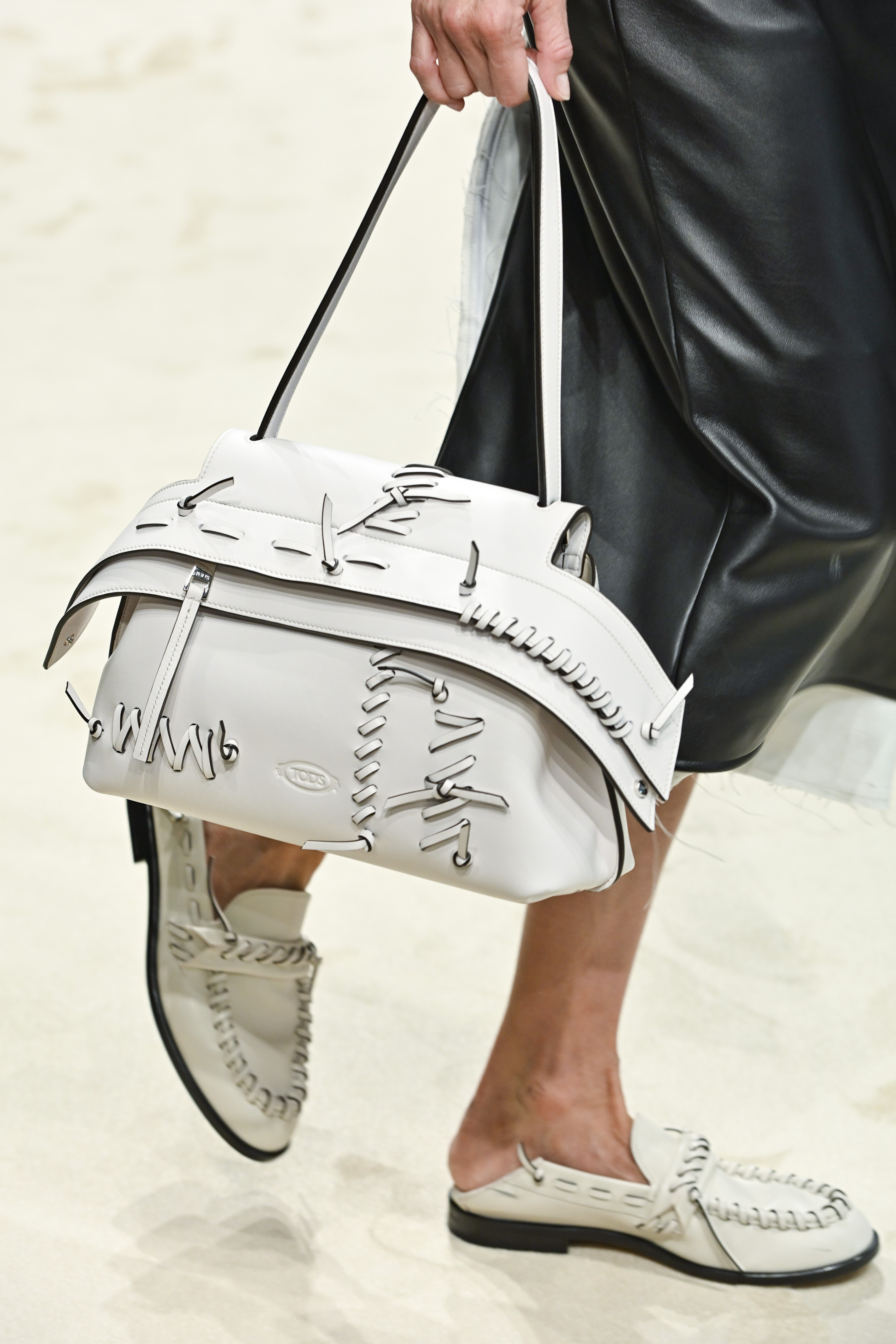 A model wearing white backless loafers and holding a white bag