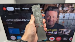 TCL C855K 65-inch Mini LED TV remote held in hand with Jamie Oliver on screen