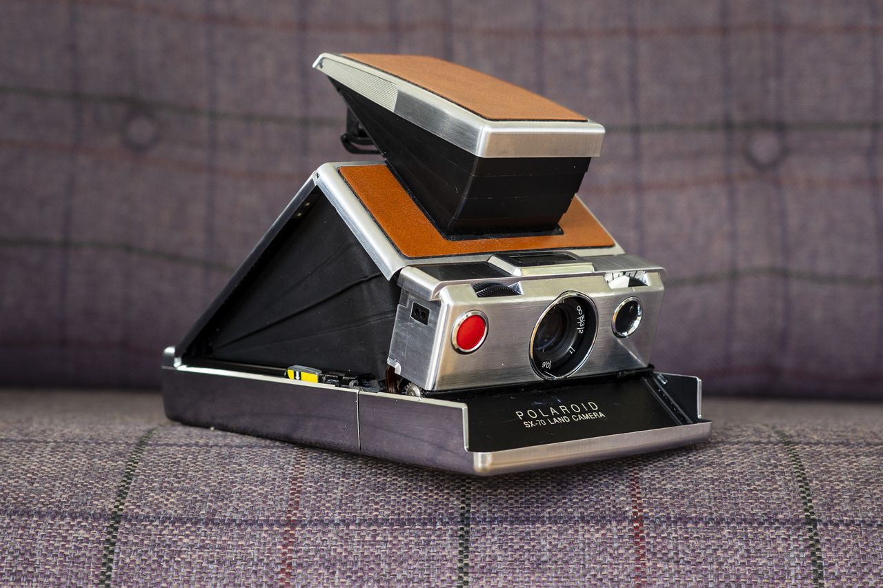 Polaroid SX70 camera front view and open in shooting position on purple chair