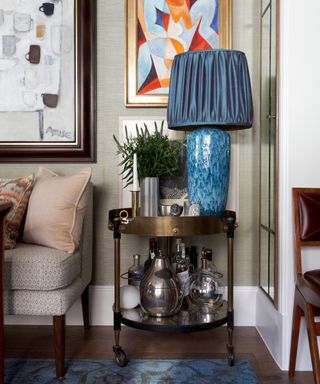 living room with mixture of artworks on the wall and metallic side table with large table lamp
