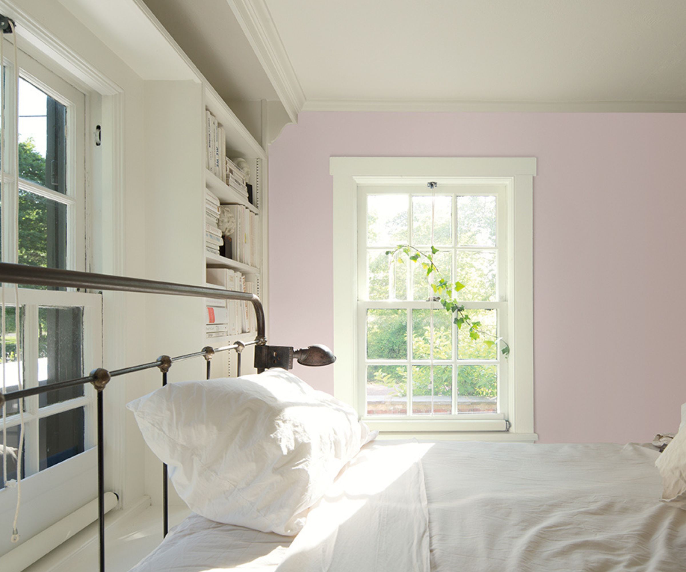 Bedroom with lilac painted wall, white ceiling, white window and white bookshelves with black iron bed and white bedding