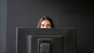 Office Worker Sneaking a Peek Above Laptop in a Modern Workspace During Daytime, hiding from boss.