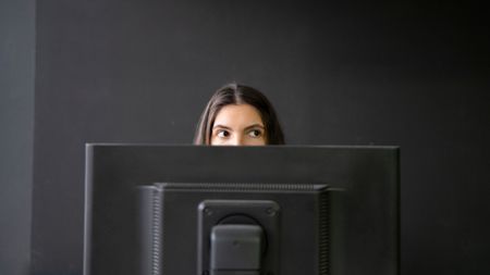 Office Worker Sneaking a Peek Above Laptop in a Modern Workspace During Daytime, hiding from boss.