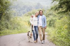 An older, happy couple walks their dog on a country road.