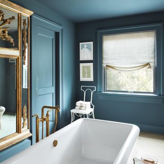 Blue colour drenched bathroom with statement gold framed mirror and white freestanding bath