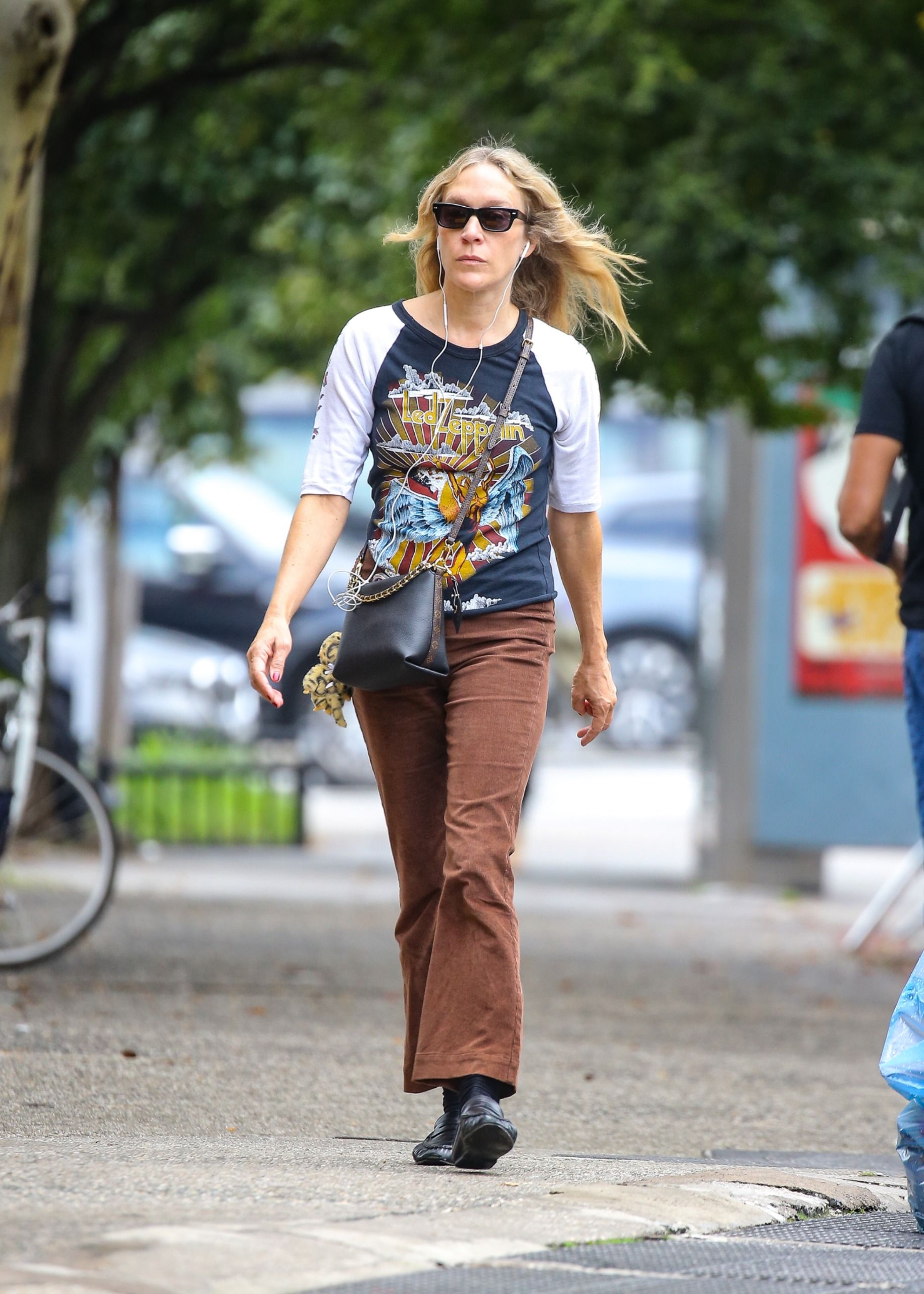 Chlo&euml; Sevigny walks outside wearing a ringer graphic t-shirt with brown kick-flare jeans and a cross-body bag.