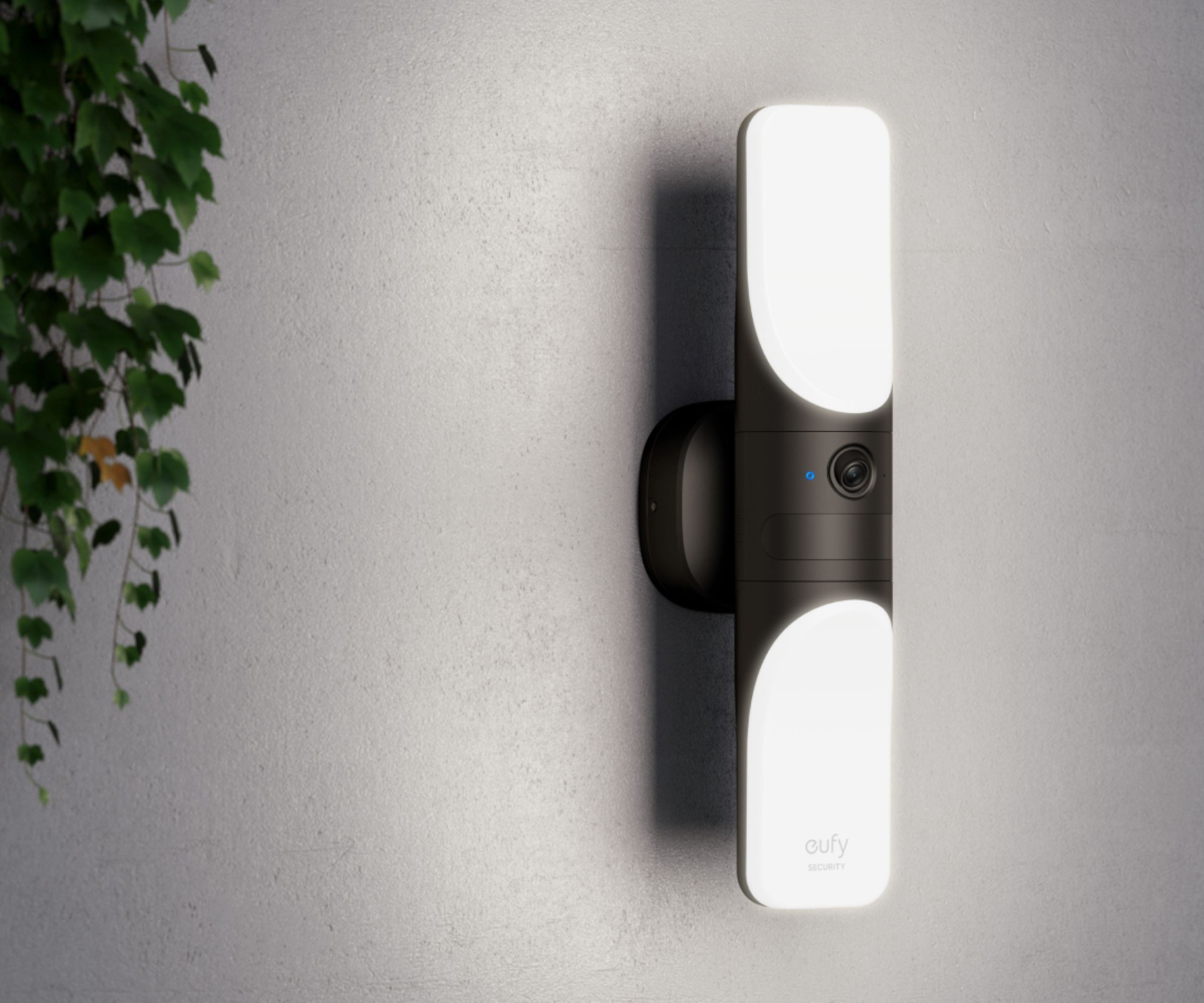 A Eufy wall light camera hung on a white wall with a plant to the left of the image