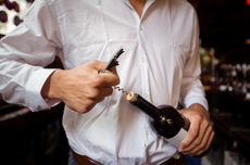 Man in white shirt opening bottle of wine with corkscrew