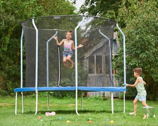 two children playing on a trampoline on a lawn with safety net