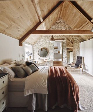 Bedroom with wooden floor, rattan rug, double bed below vaulted ceiling.
