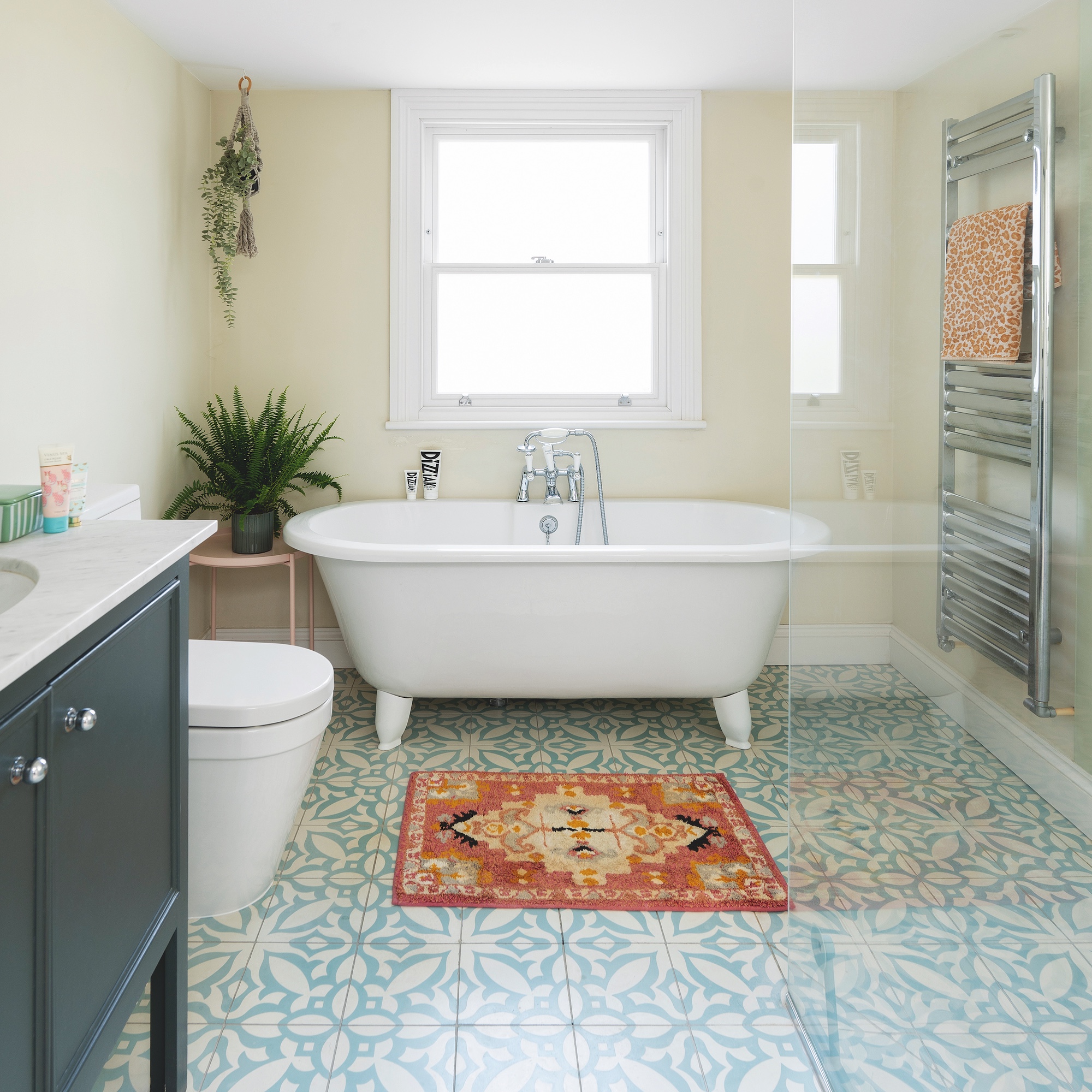 bathroom with white freestanding bath, blue and white patterned floor tiles, small square rug and grey vanity unit