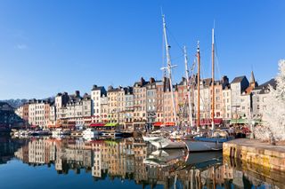 Honfleur harbour in Normandy, one of the best foodie cities in France. Colorful apartments and restaurants and their reflection in the harbour water, where sail boats float