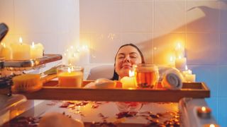A woman meditating in the bath surrounded by candles.
