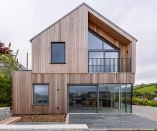 Contemporary timber-clad self build with a pitched roof, and an interesting triangular window on the first floor and a glazed corner on the ground floor