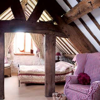 bedroom with wooden beams metal bed red and white armchair wooden flooring