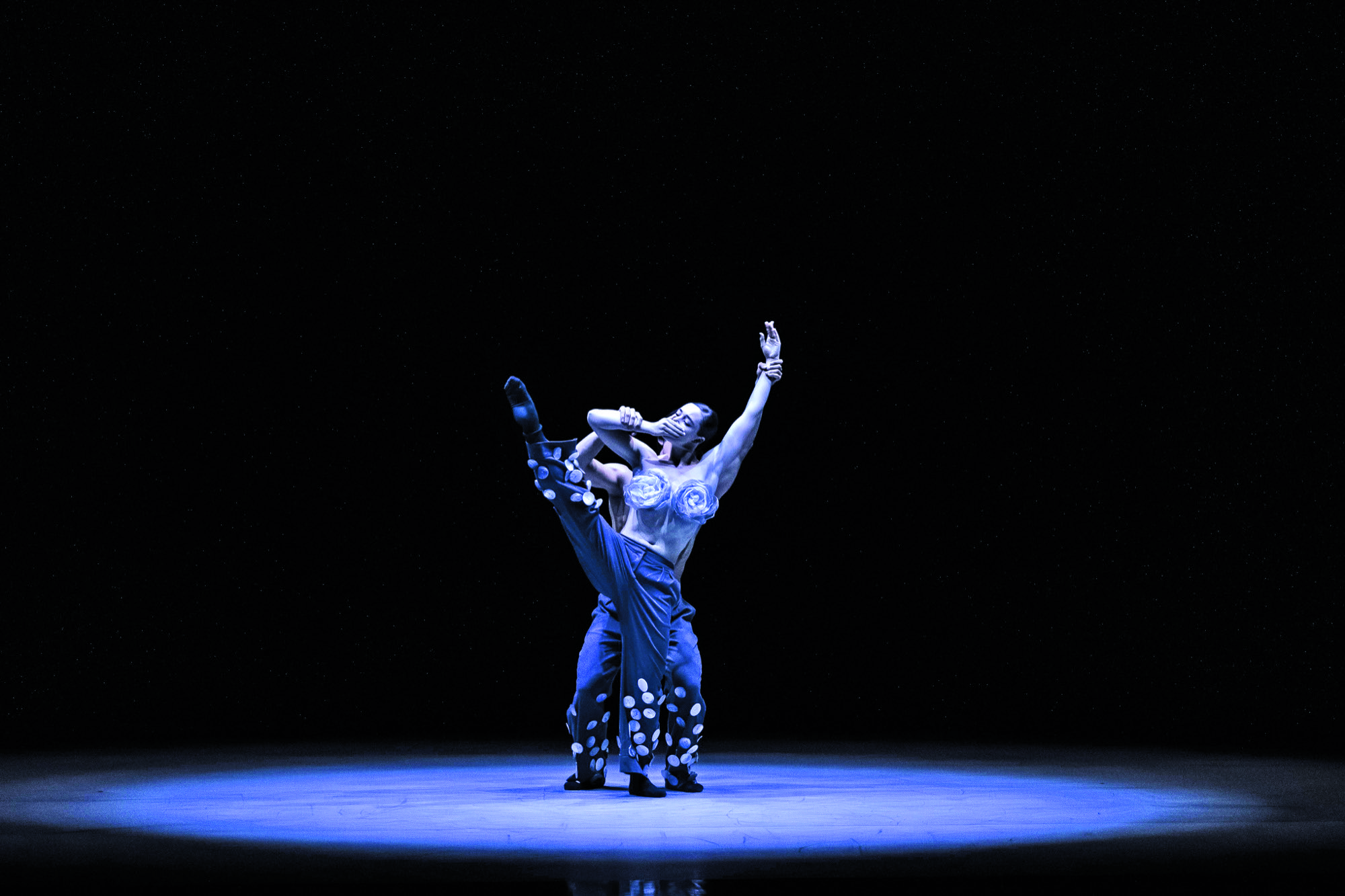 Two dancers are intertwined on a dark stage in a ballet maneouvre