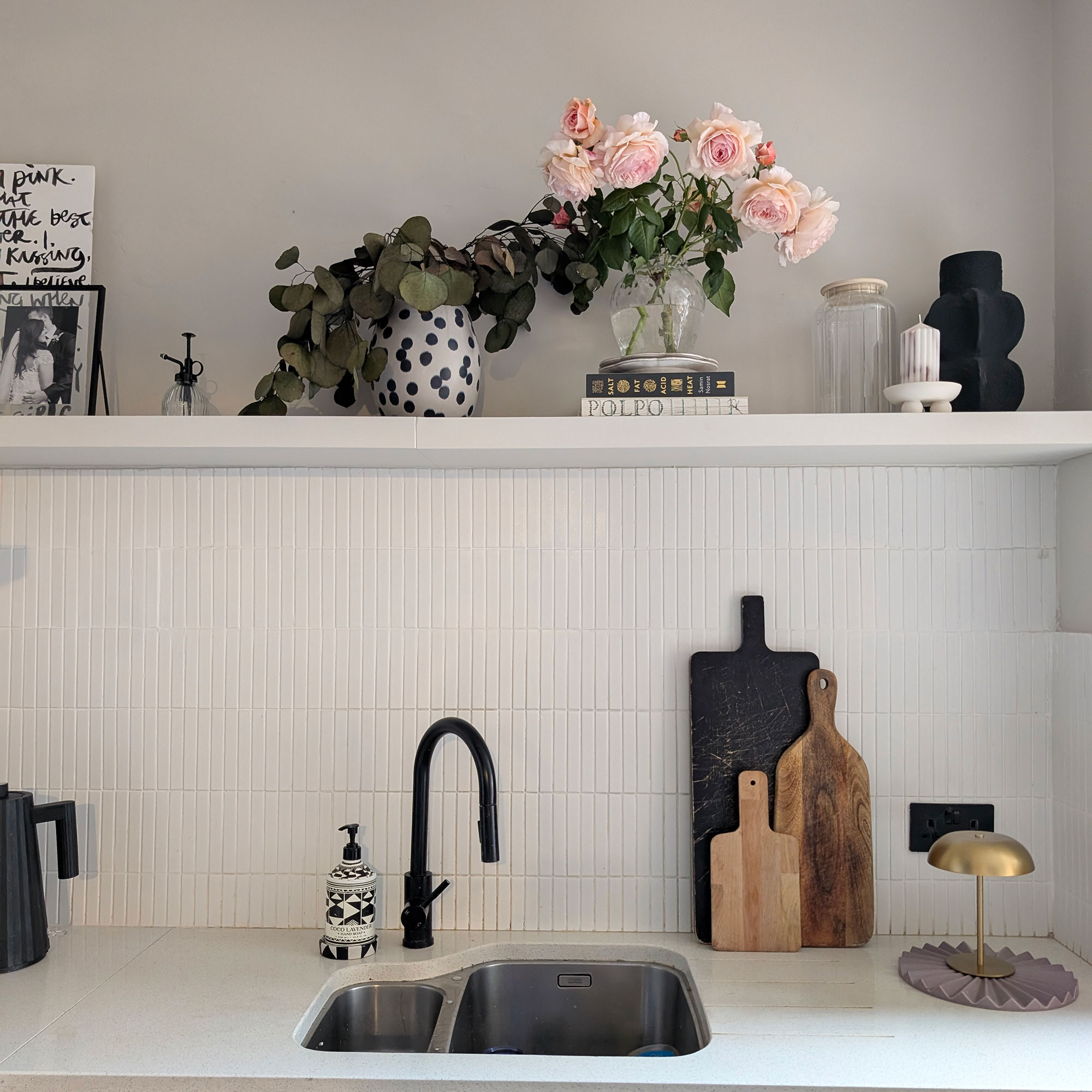 White kitchen with floating shelf above sink holding books, roses and houseplant