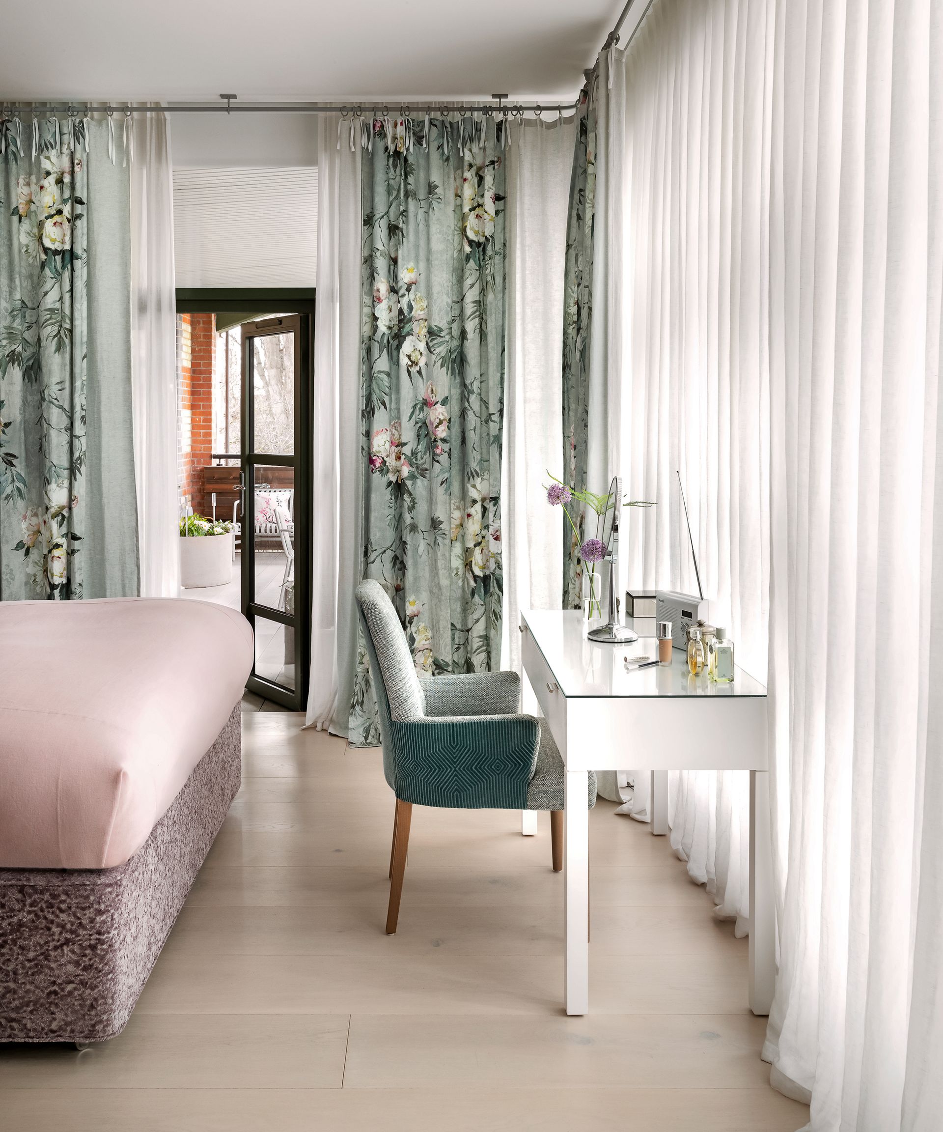 A bedroom with a dressing table, pink bed and printed floral curtains
