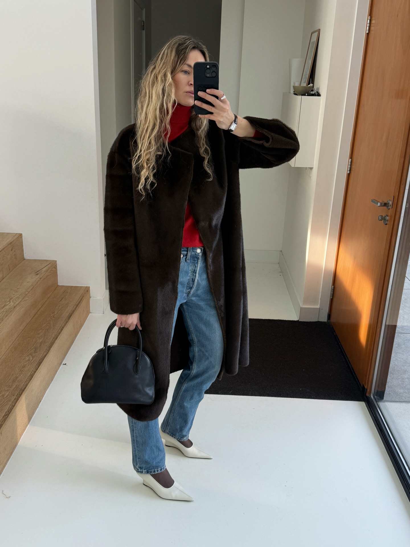 Woman wearing a long black coat, a red sweater, and jeans.