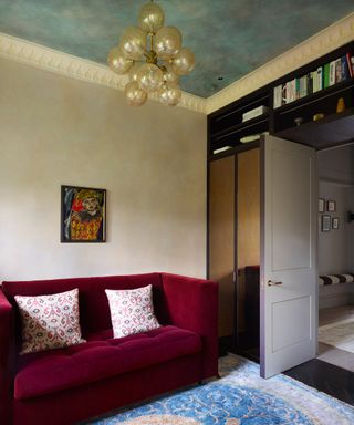 Living room red velvet sofa and Persian inspired rug, painted blue mural on ceiling