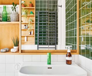 Shot of sink with green tap, mirror and built-in oak shelving, white square splashback tiles and deep green wall tiles