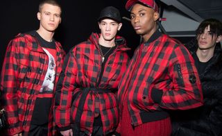 Three models in red/black check coats and one more person to the right in all black