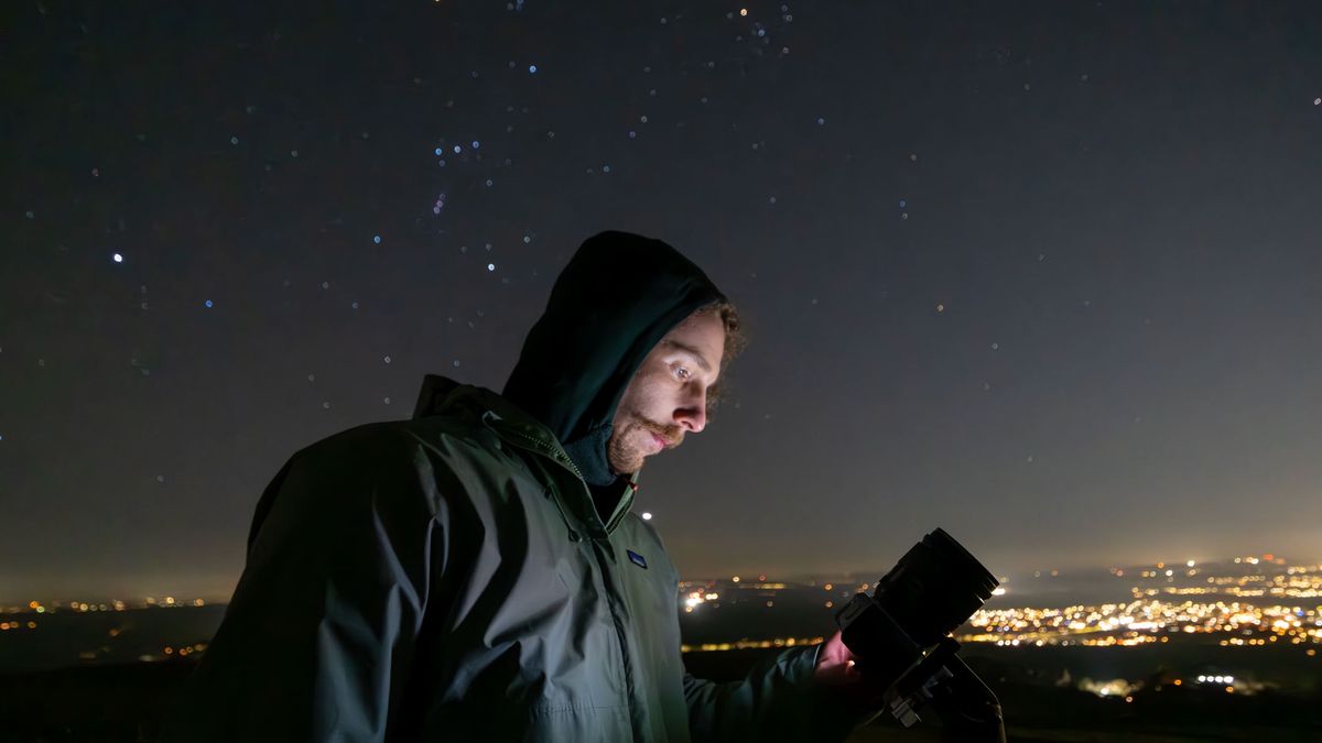 A man looking at the Fujifilm X-M5 at night with Orion's Belt and city lights in the background
