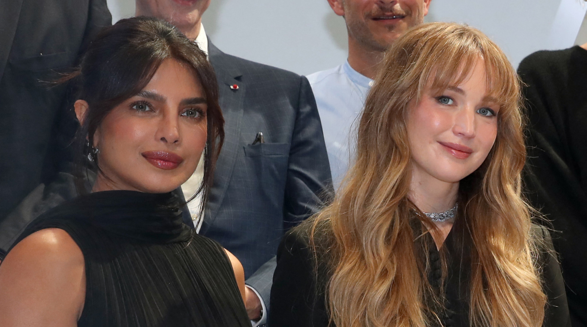 Jennifer Lawrence has long blonde hair and is wearing a black Dior suit, Priyanka Chopra wears her black hair tied back and wears a black Dior dress with a white tiered skirt
