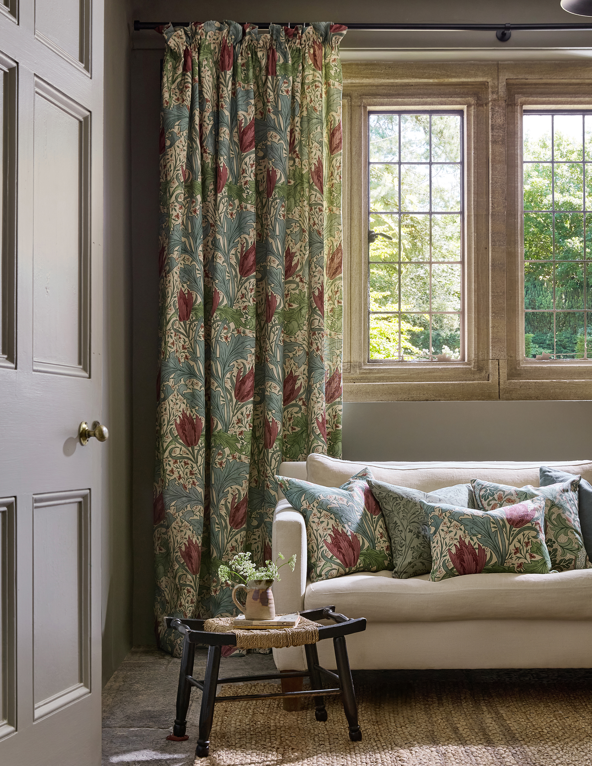 A sofa with Morris & Co. pillows on it in front of a Morris & Co. curtain