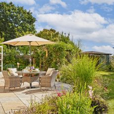 a patio with dining furniture and parasol alongside a lawn and summerhouse